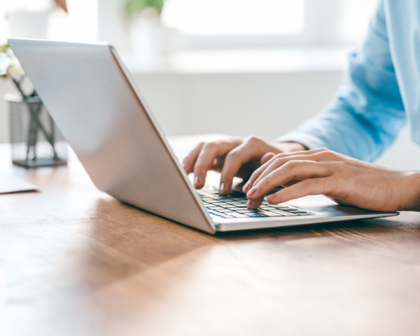 Person tippt auf Laptop-Tastatur in heller Umgebung.