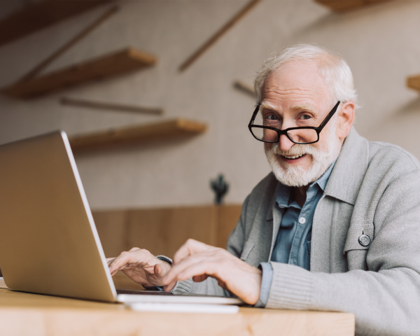 Älterer Mann mit Laptop und Brille lächelt – Kontaktaufnahme leicht gemacht