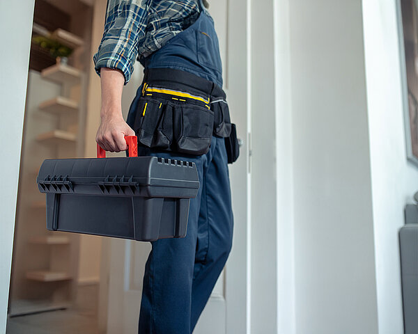 Handwerker mit Werkzeugkoffer und Arbeitskleidung betritt ein Haus zur Installation.