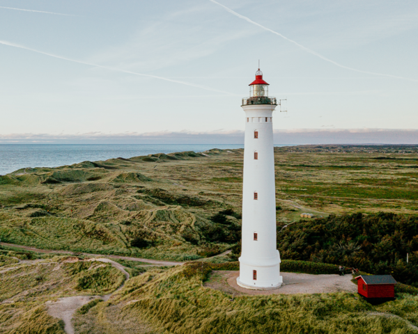 Weißer Leuchtturm an der Küste mit Blick aufs Meer und hügelige Dünenlandschaft