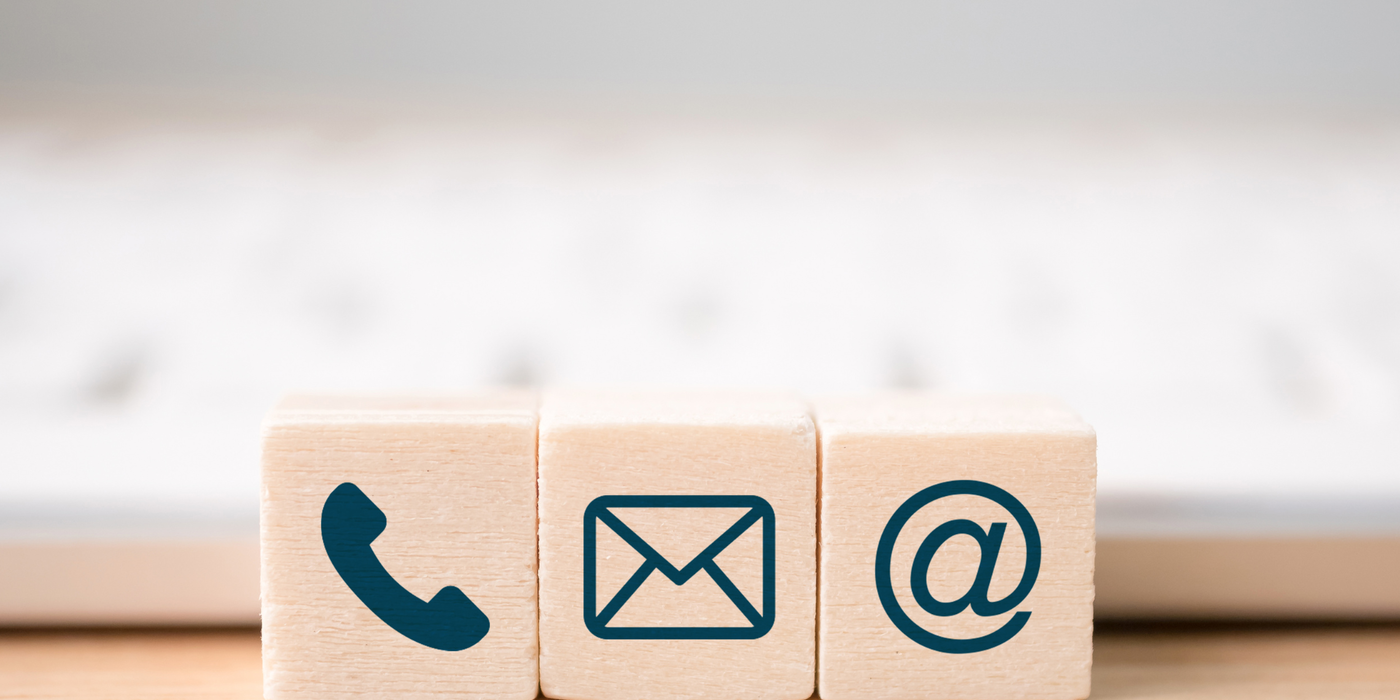 Drei Holzklötze mit Symbolen für Telefon, E-Mail und Internet stehen vor einer Tastatur als Zeichen für Kontaktmöglichkeiten