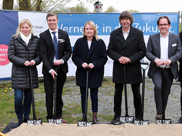 Projektverantwortliche stehen mit Spaten in der Hand vor einem Sandhaufen