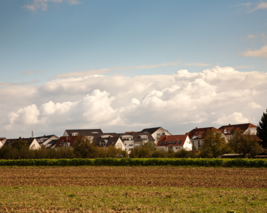 Mehrfamilienhäuser am Feldrand unter blauem Himmel – Glasfaser für ländliche Wohnanlagen