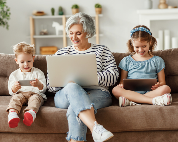 Oma sitzt mit ihren Enkeln vor dem Laptop auf der Couch