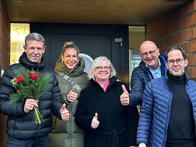 Projektverantwortliche stehen vor einer Haustür und freuen sich