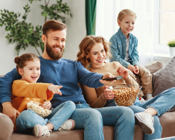 Familie sitzt auf dem Sofa, der Vater hat eine Fernbedienung in der Hand