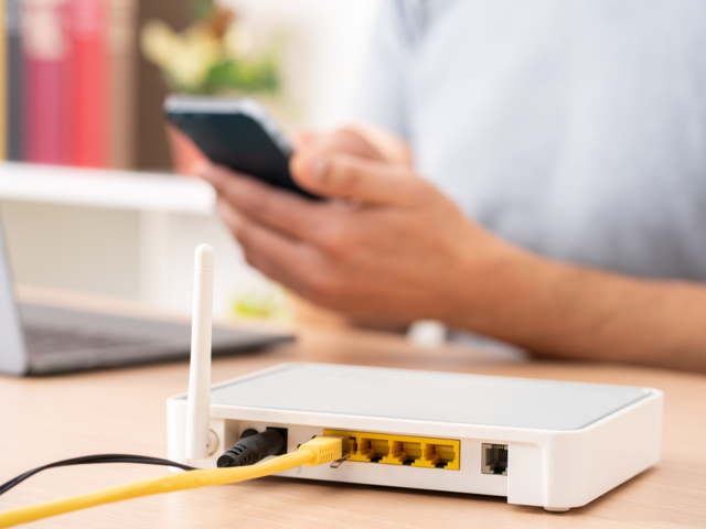 Nahaufnahme von einem Router, im Hintergrund sind Hände, die ein Handy bedienen